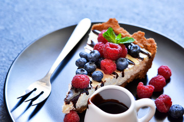 Homemade vanilla cheesecake with chocolate sauce and berries on a concrete background.