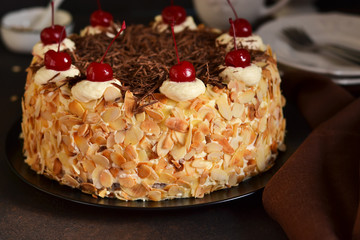 Chocolate cake with vanilla cream, cherry and almonds on a dark background.