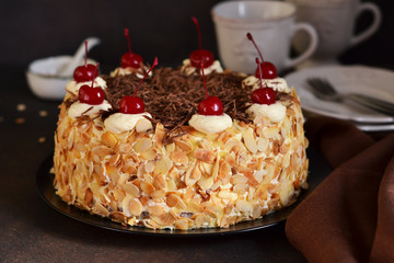 Chocolate cake with vanilla cream, cherry and almonds on a dark background.