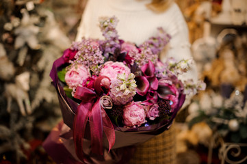 Woman holding a bouquet with pink, violet and crimson flowers wrapped in dark color paper