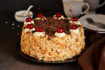 Chocolate cake with vanilla cream, cherry and almonds on a dark background.