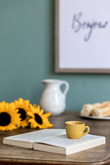 Obraz na płótnie Canvas Stylish and cozy interior of kitchen space with wooden table beautiful sunflowers, cup of coffee, book and flower. Scandinavian decor of interior with kitchen accessories. Template. 