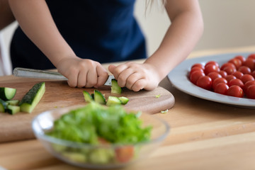Little girl chopping cucumber with knife, cooking salad close up