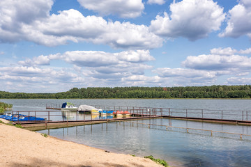 pier on sand shore of a large lake in summer day with beautiful clouds.  sky reflection