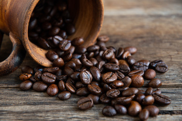 Roasted coffee beans scattered on old boards from a ceramic folk cup.