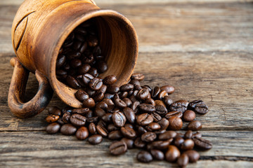 Roasted coffee beans scattered on old boards from a ceramic folk cup.