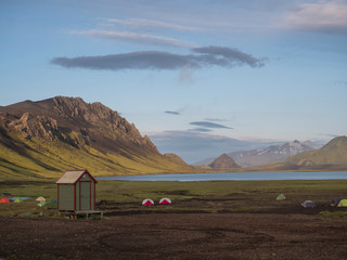 Colorful tents at camping site on blue Alftavatn lake with green hills and glacier in the otherwordly beautiful landscape of the Fjallabak Nature Reserve in the Highlands of Iceland part of famous