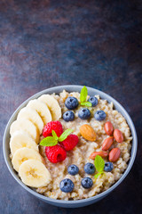 Healthy breakfast. Oatmeal with blueberries, banana and raspberry. Oatmeal with fruits and nuts in a bowl. Cooked oatmeal on dark background. Vegetarian food