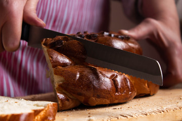 Hands of old woman  cutting a tasty loaf of bread on a wooden board.  Fresh traditional bread is on table close-up. Fresh bread on the kitchen table