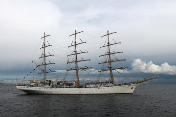 Fototapeta na wymiar Training sailing frigate goes to sea from the port of Gdynia against a stormy sky