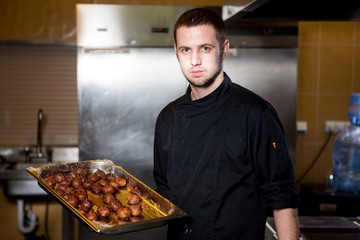 Portrait male chef with cooked food standing in kitchen. Theme cooking. young Caucasian man in black uniform, latex gloves at restaurant in kitchen. dish of figs, fig fruit fig tree or Ficus Carian