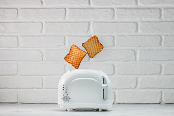 Roasted toast bread popping up of toaster with white brickwall