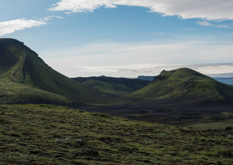 Fototapeta premium Volcanic landscape with blue container,Tindfjallajokull glacier, green hills and lava gravel ground covered by grass and moss. Fjallabak Nature Reserve, Iceland