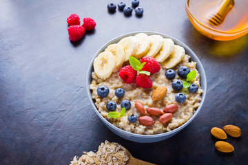 Healthy breakfast. Oatmeal with fruits, nuts and honey. Oatmeal with blueberries, banana and raspberry. Cooked oatmeal on dark background. Vegetarian food