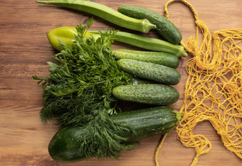 Fresh green vegetables next to a yellow string bag on a brown wooden background, top view