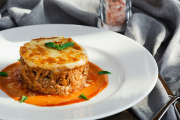 Close-up of a traditional lasagna made with minced beef bolognese sauce topped with basil leafs served on a white plate