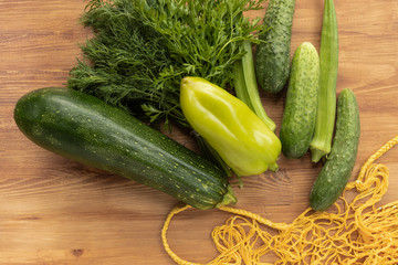 Fresh green vegetables next to yellow string bag on brown wooden background