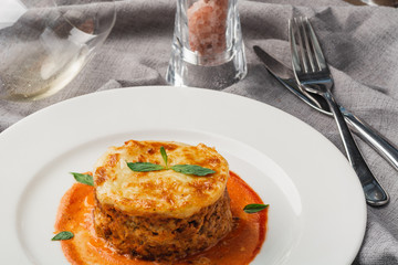 Close-up of a traditional lasagna made with minced beef bolognese sauce topped with basil leafs served on a white plate