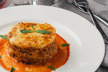 Close-up of a traditional lasagna made with minced beef bolognese sauce topped with basil leafs served on a white plate