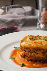 Close-up of a traditional lasagna made with minced beef bolognese sauce topped with basil leafs served on a white plate