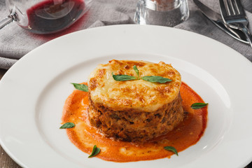 Close-up of a traditional lasagna made with minced beef bolognese sauce topped with basil leafs served on a white plate