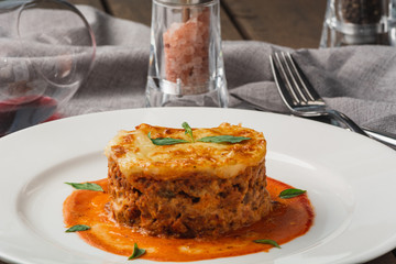 Close-up of a traditional lasagna made with minced beef bolognese sauce topped with basil leafs served on a white plate