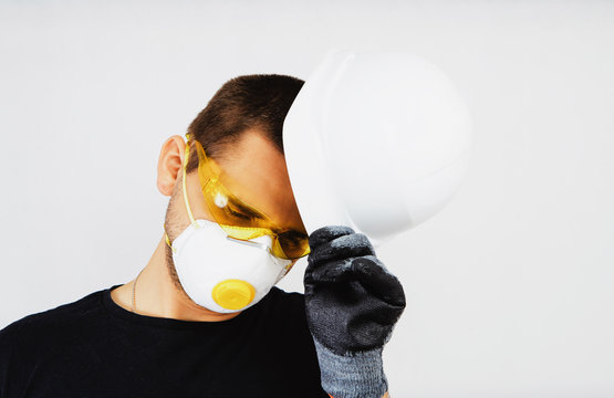 A worker wearing a protective helmet, protective goggles and a protective mask pulls the helmet off his head. Work concept, hiring workers for construction. Preparation to work. - Powered by Adobe