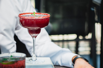 Raspberry Margarita in chilled glass over light background on reflection surface, garnished with fresh mint. Most popular cocktails series.