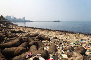 Mumbai shoreline is filled with heap of garbage/plastic, modern city buildings and Haji Ali Dargah...