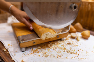 Women's hands cut bread with a bread cutter. The girl cuts French long bread into pieces with a special knife
