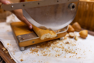 Women's hands cut bread with a bread cutter. The girl cuts French long bread into pieces with a special knife