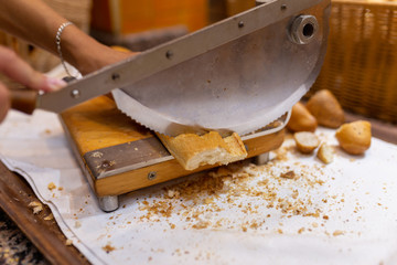 Women's hands cut bread with a bread cutter. The girl cuts French long bread into pieces with a special knife