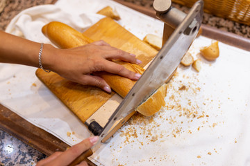 Women's hands cut bread with a bread cutter. The girl cuts French long bread into pieces with a special knife