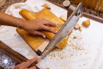 Women's hands cut bread with a bread cutter. The girl cuts French long bread into pieces with a special knife