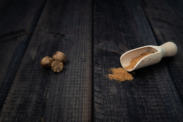 Ground and whole nutmeg with a scoop on a dark wooden countertop. The concept of eating and adding spices to dishes. Improving the taste of dishes, sharp expressive taste.
