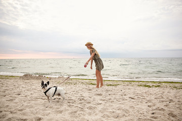 Horizontal outdoor shot of pretty young woman with blonde hair walking along beach on overcast with...