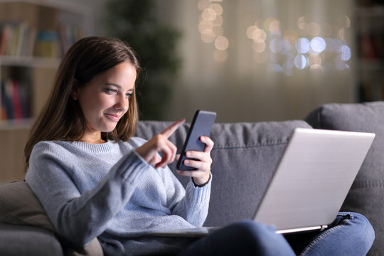 Satisfied woman using phone and laptop in the night