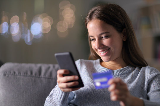 Happy woman buying with phone and credit card at home