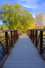 Wooden bridge with metal rails on water with beautiful fall colors on a sunny day
