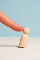 A finger pokes into a wooden figure on a blue background. Concept fired. Staff reduction. Close up.