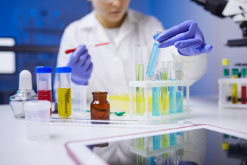 Close up of unrecognizable female scientist holding test tube with colored liquid while working on medical research in laboratory, copy space