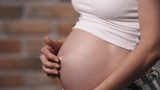 Close-up pregnant woman with baby moving and kicking inside belly, future mother indoors in living appartment carefully touch tummy and playing with her baby. Last trimester of pregnancy