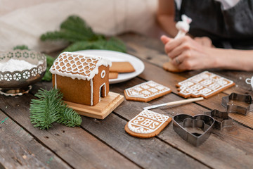 A lot of ginger biscuits in the form of European houses on brown wooden table. Decorated with white sweet glaze. Christmas mood, winter morning.