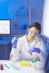 Portrait of young female scientist preparing blood test sample using dropper while working in medical laboratory