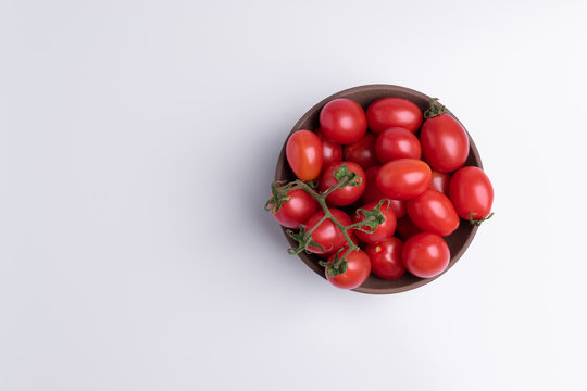 Grape or cherry tomato branch. Pile of red grape tomatoes in a brown bowl, isolated on white background