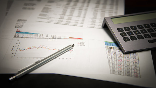 Financial business reports on a desk with a pen and calculator