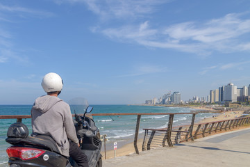 Fototapeta premium A man in a helmet sits on the seat of his motorcycle and looks at the panorama of the coastal city.