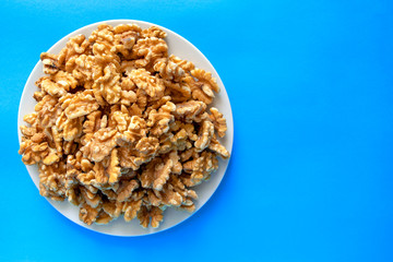 Pile of walnuts on white plate isolated on blue background. Healthy snack and food. Top view. Walnuts