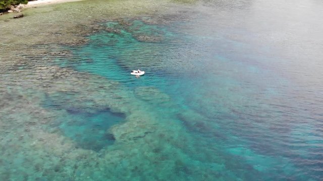 aerial view of a people snorkeling from a small dingy through coral reef in the south pacific