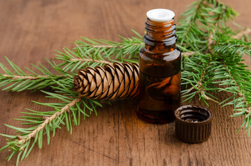 bottle of fir tree essential oil on wooden background with pine cone